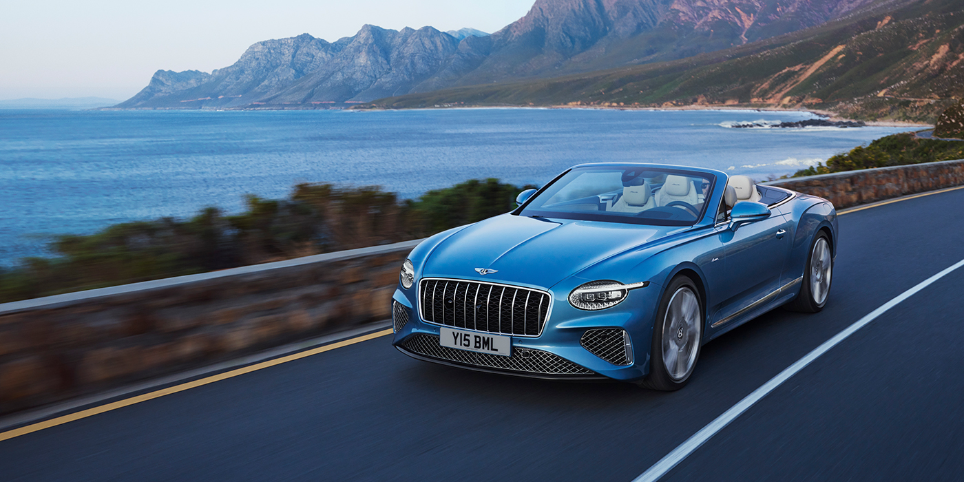 Bentley Almaty New Bentley Continental GTC Azure convertible in Light Windsor blue paint with 22 inch Azure wheels and chrome grill, driving dynamically by the sea