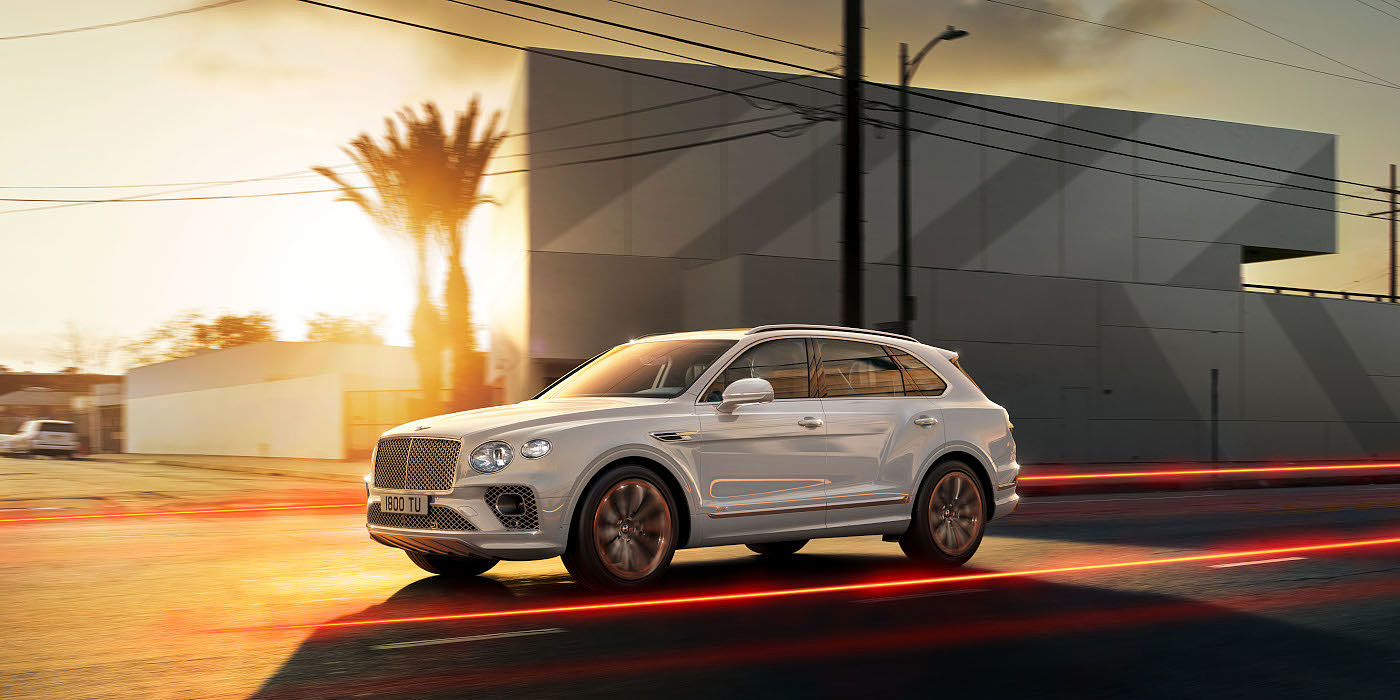 new-bentley-bentayga-hybrid-in-ice-white-paint-front-three-quarters-driving-past-buildings-in-los-angeles