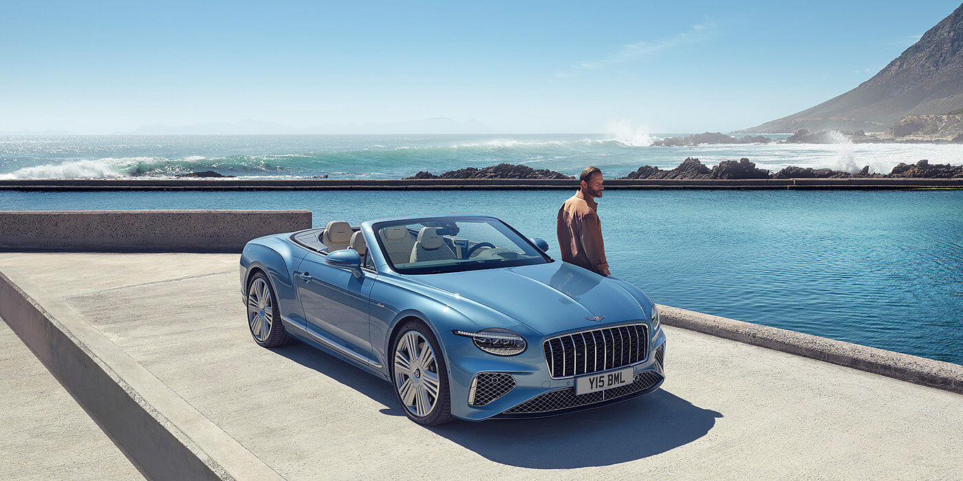 Bentley Almaty New Bentley Continental GTC Azure convertible front view in Light Windsor blue paint with 22 inch ten spoke wheels parked by the sea in the sunshine