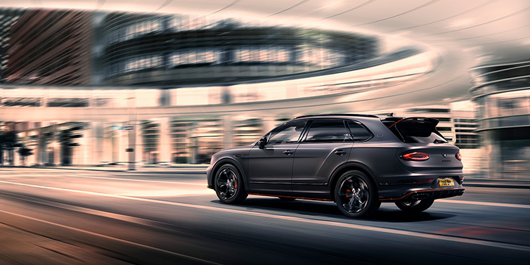 Bentley Almaty Bentley Bentayga S Black Edition SUV rear three quarter in Anthracite Satin paint driving dynamically through a city at night