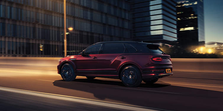 Bentley Almaty Bentley Bentayga Extended Wheelbase Mulliner SUV in Cricket Ball red paint driving dynamically in city at night